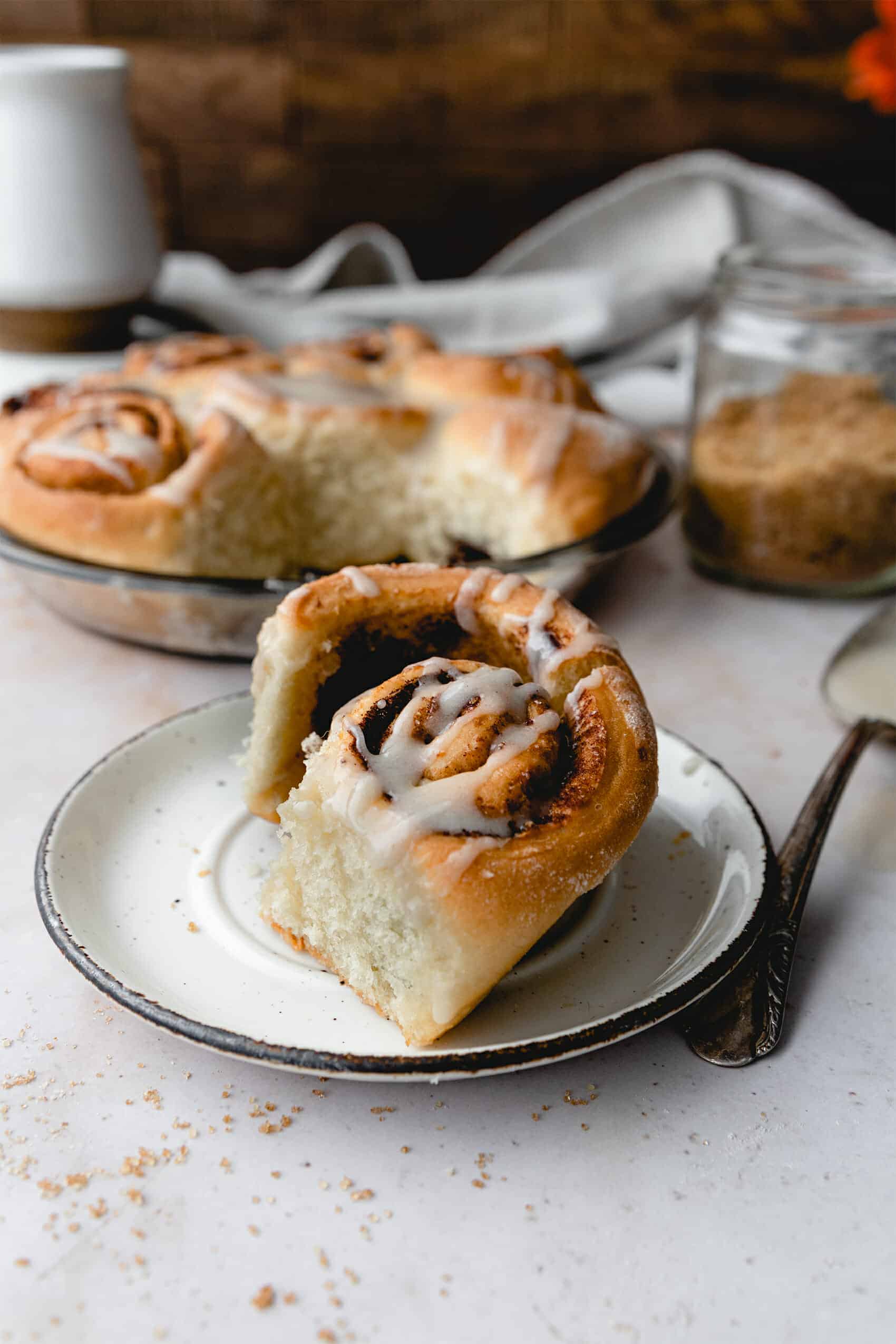 side view of cinnamon roll on a white plate with a plate of more in the background