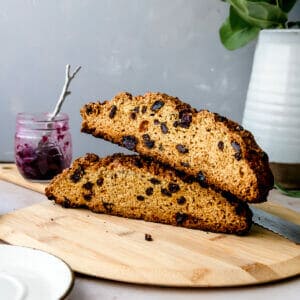 irish soda bread cut in half on a wooden board with a blueberry jam in the background