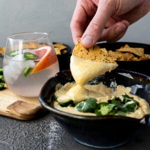 hand holding a tortilla chip dipping into a bowl of creamy 3 ingredient vegan queso