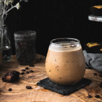 side view of iced coffee shake on a wooden table next to some coffee beans