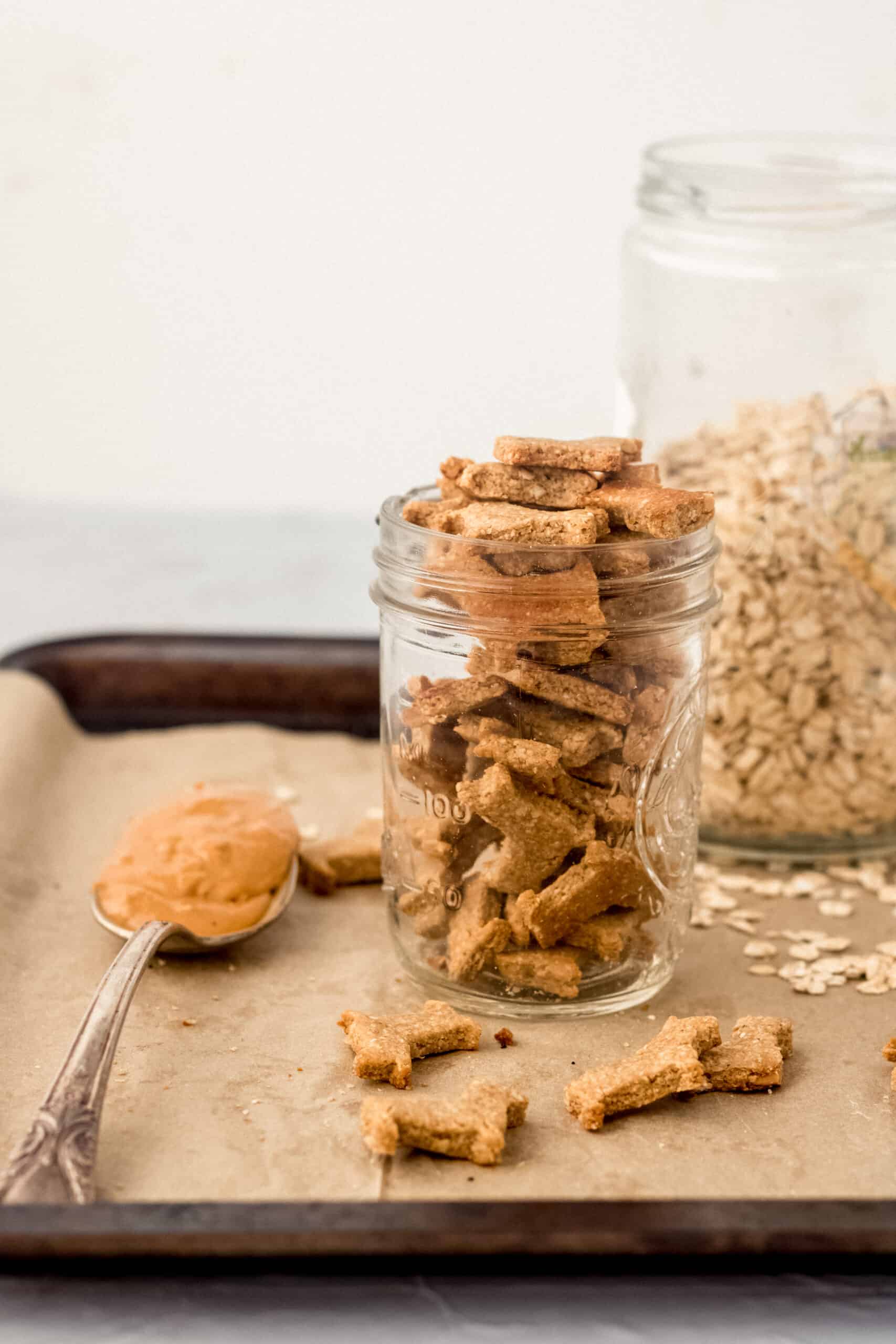 glass jar of homemade dog treats on a tray with a spoon of peanut butter