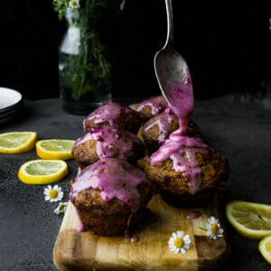 hand holding spoon pouring glaze onto vegan lemon poppyseed muffins on a wooden trayolding spoon pouring glaze onto vegan lemon poppyseed muffins