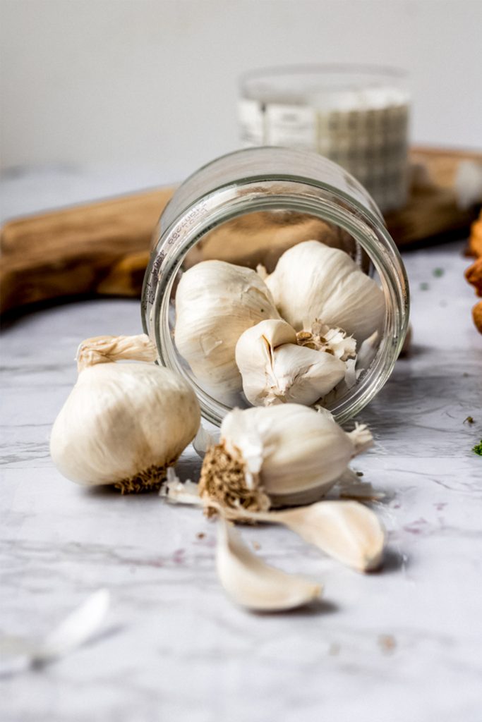 jar of garlic heads turned on its side on marble table