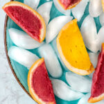 two raspberry and one mango sorbet orange wedge on a blue plate of ice