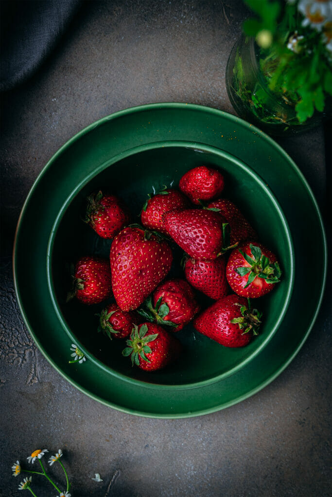green bowl of strawberries on a green plate