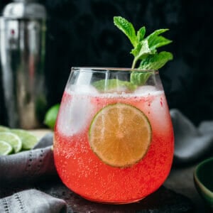 side view of strawberry limeade with a lime circle and a sprig of mint