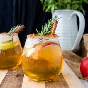 smoky apple cider sangria with cinamon, apple slices, and rosemary on a wood board