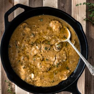 cast iron skillet with vegan gravy with mushrooms on a striped wooden board