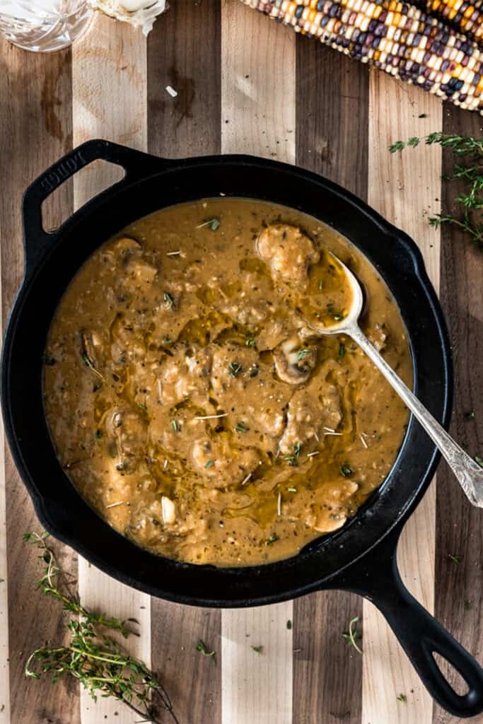 cast iron skillet with vegan gravy with mushrooms on a striped wooden board