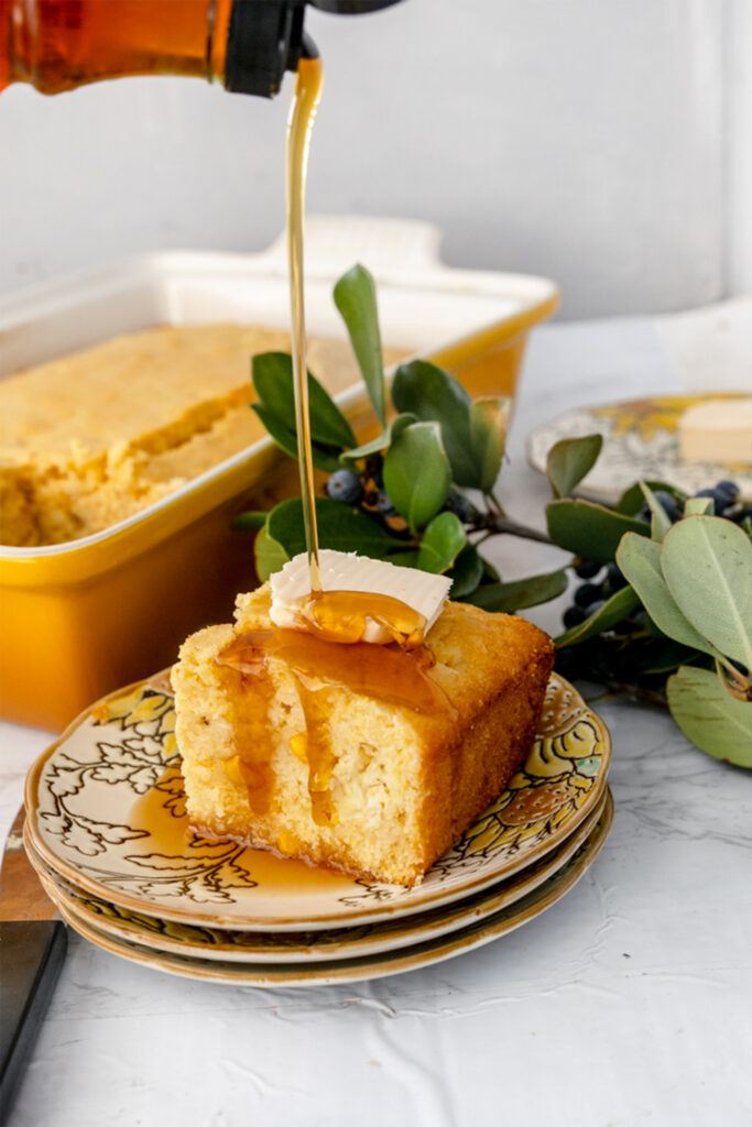 slice of fluffy cornbread on a plate with a pour of maple syrup