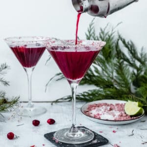 red clausmopolitan pouring into martini glass out of a silver shaker