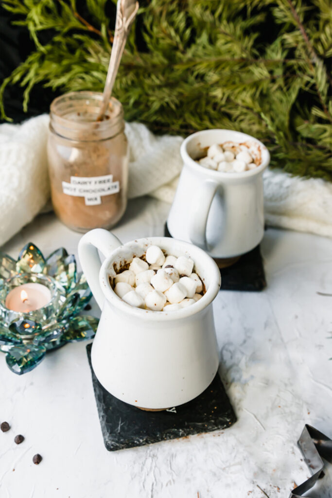 two mugs of dairy-free hot chocolate on a marble board with a candle