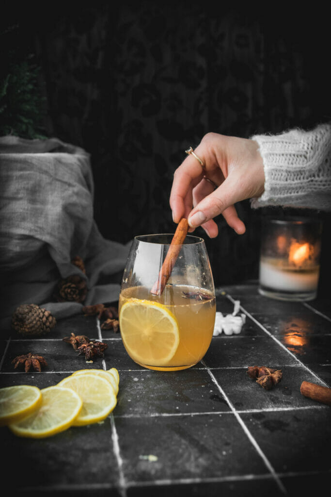 hand reaching into frame to stir a hot toddy with a cinnamon stick