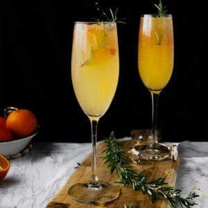 two flutes of orange mimosa cocktail on a wooden board