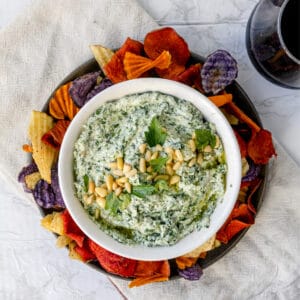 Overhead shot of spanakopita dip in a white bowl surrounded by colorful chips