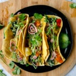 overhead shot of three kale potato tacos on a black plate on a wooden board