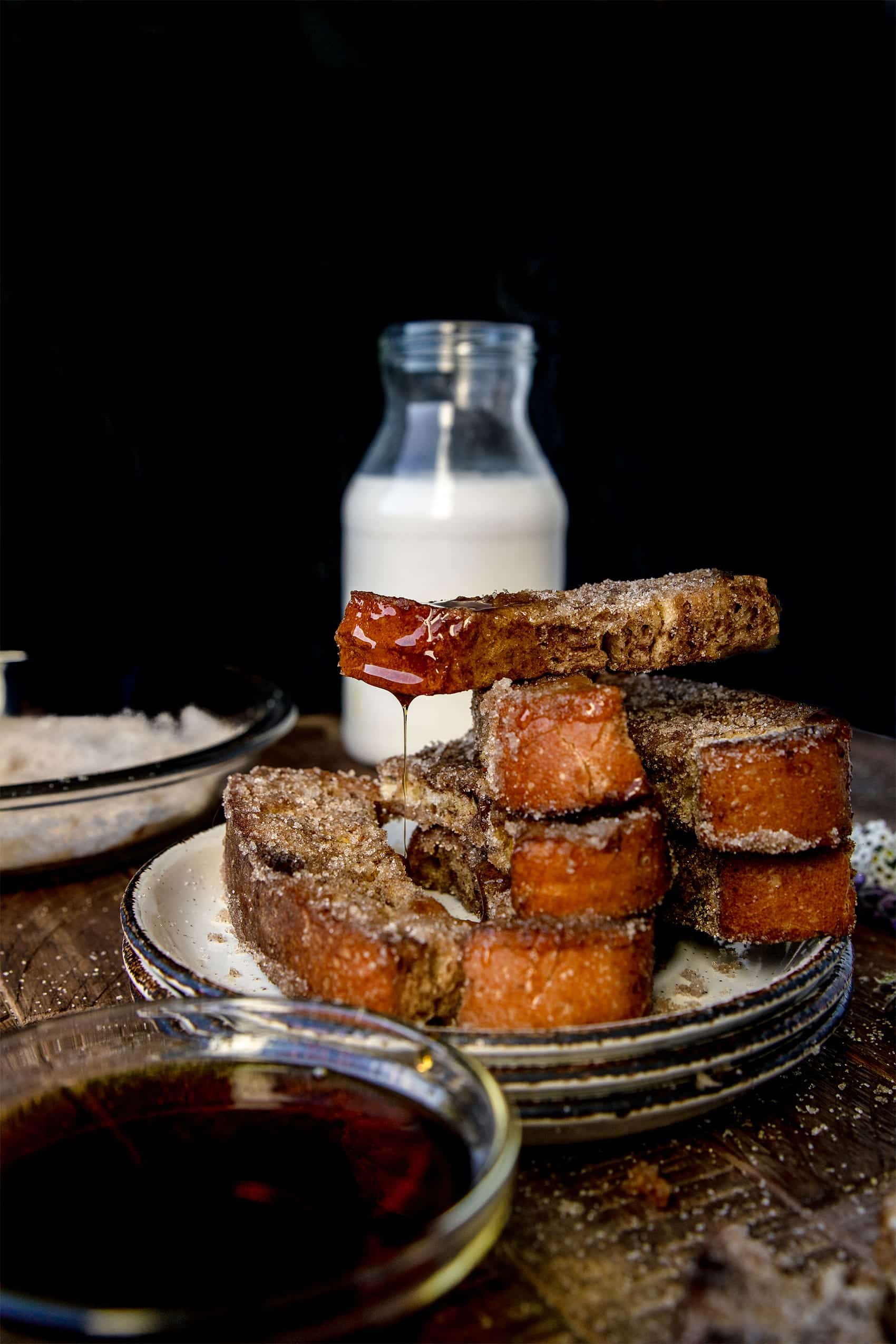 french toast stick on a stack with syrup dripping off of it onto a white plate