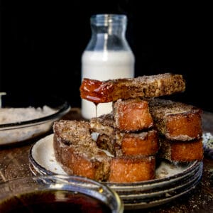 french toast stick on a stack with syrup dripping off of it onto a white plate