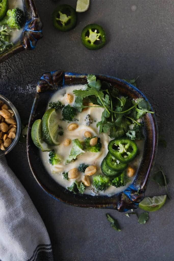 overhead shot of spicy peanut noodle soup with noodles and limes