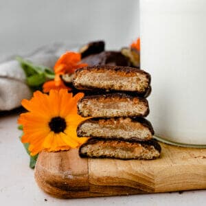 stack of peanut butter patty tagalong cookies on a wooden board, cut open so you can see the layers of cookie and peanut butter. Coated in chocolate