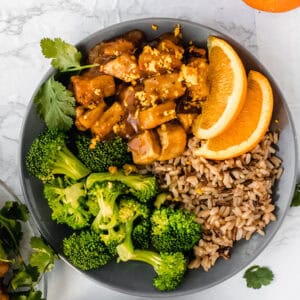 orange slices with orange tofu broccoli and rice on a grey plate