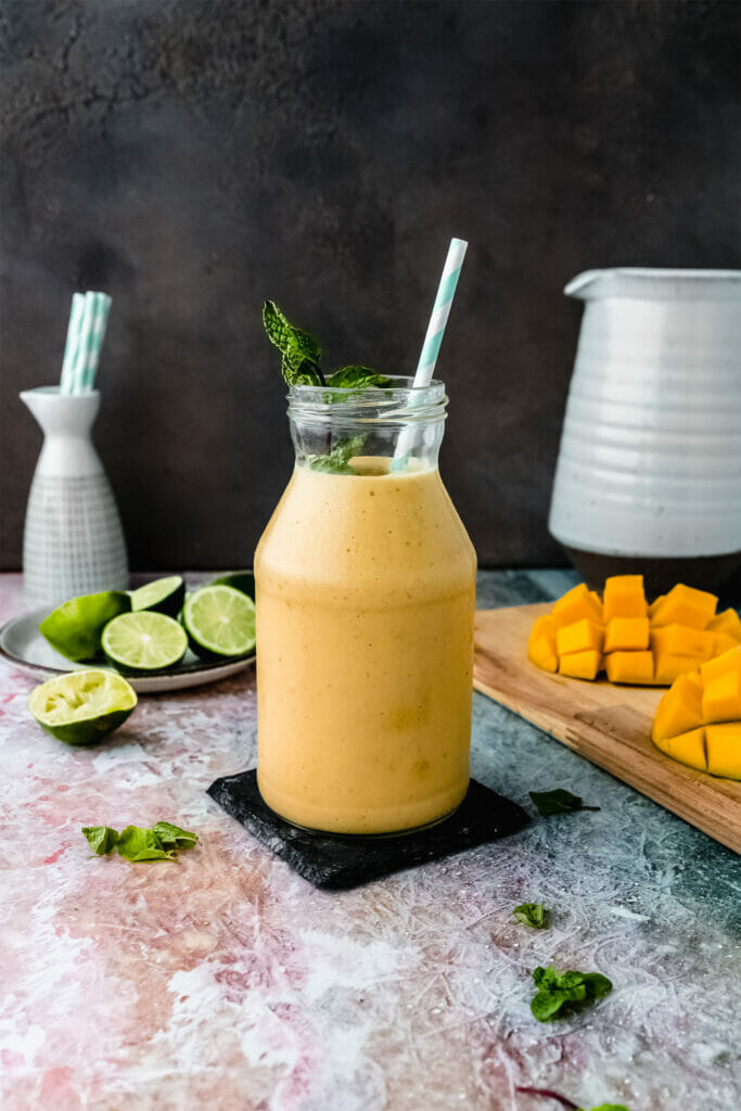 glass jar of vegan mango lassi on a table next to mango pieces