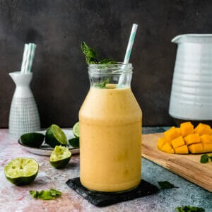 glass jar of vegan mango lassi on a table next to mango pieces