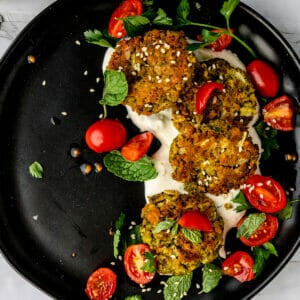 black plate with vegan pistachio baked falafel covered in cherry tomatoes and fresh herbs