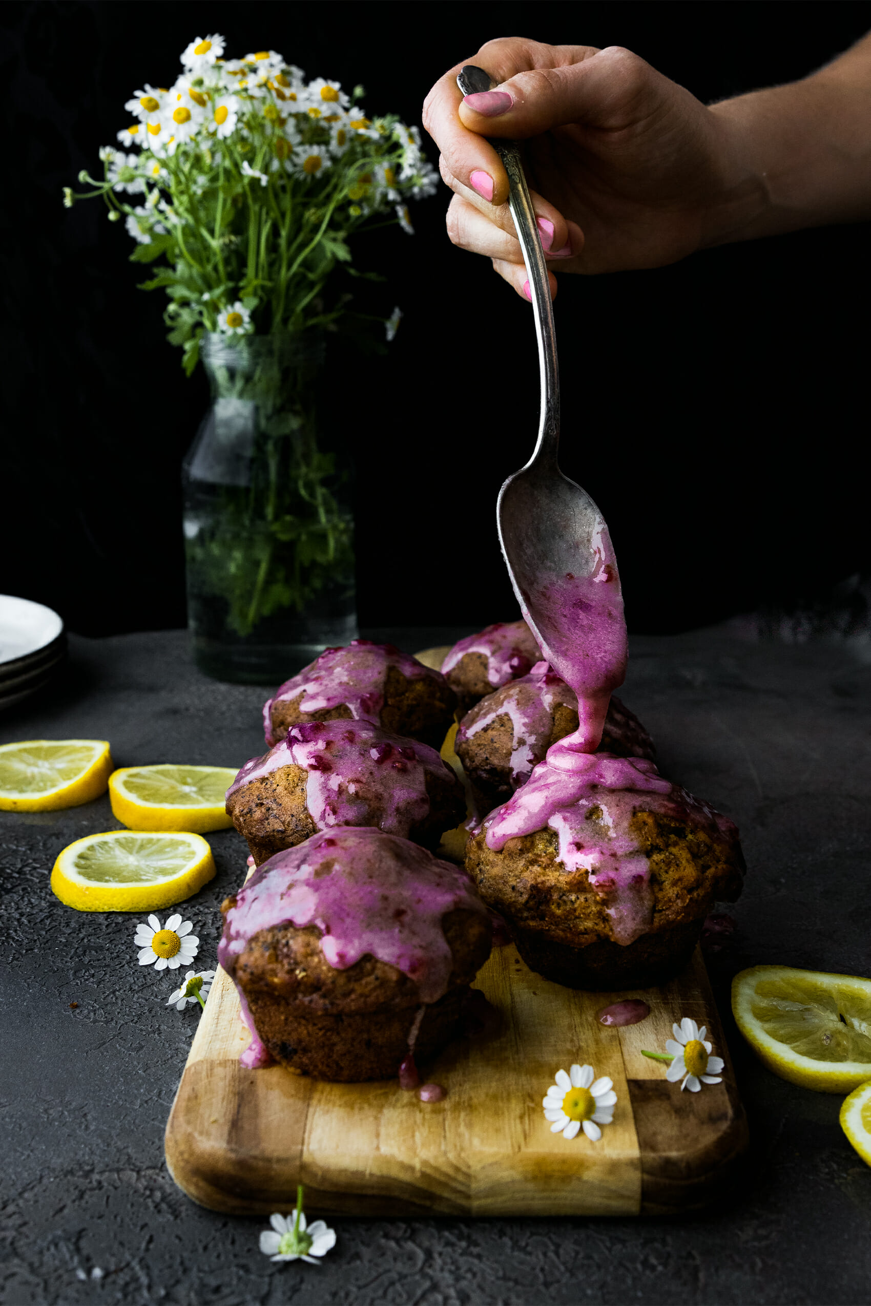 hand holding spoon pouring glaze onto vegan lemon poppyseed muffins on a wooden trayolding spoon pouring glaze onto vegan lemon poppyseed muffins