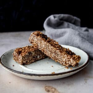 two chocolate chip chewy bars on a white plate next to a cloth on a marble table