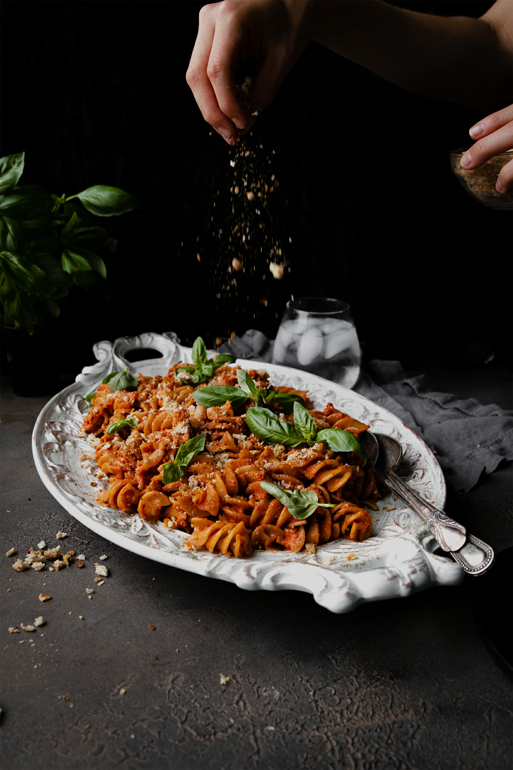 hand holding breadcrumbs sprinkled onto a plate of roasted red pepper pasta salad