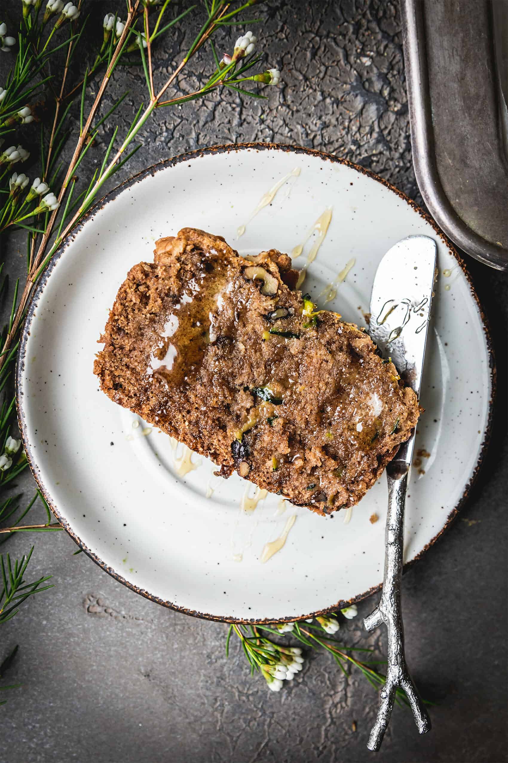 overhead shot of plant based zucchini bread on a white plate next to a silver knife