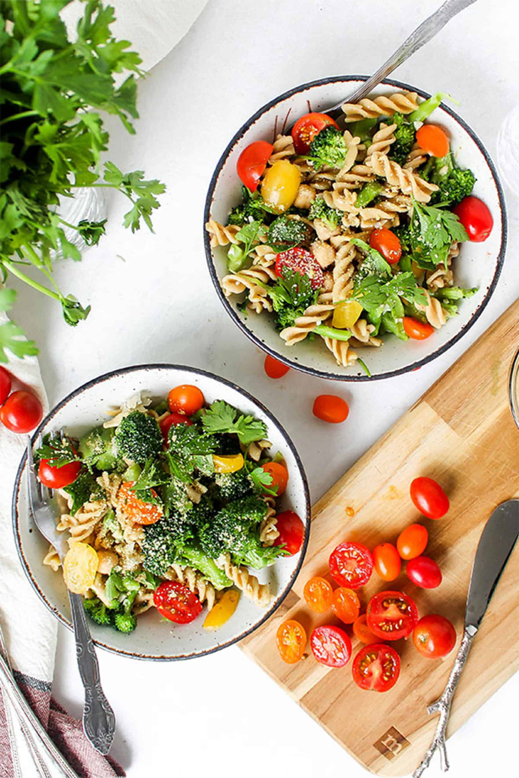 two bowls of vegan broccoli garlic pasta on a white table