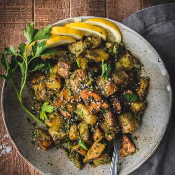 overhead shot of creamy pesto potatoes in a ceramic bowl with lemon wedges and parsley