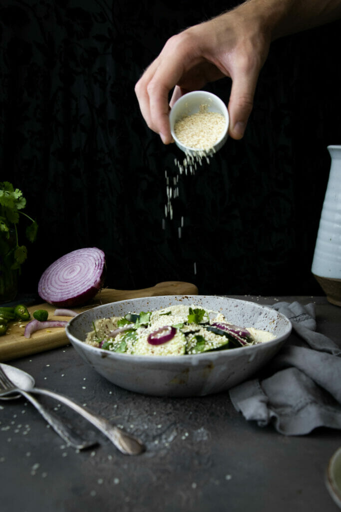 sesame seeds pouring onto a cucumber salad