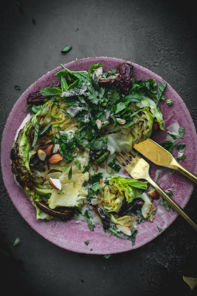 overhead shot of grilled cabbage on a pink plate with gold utensils