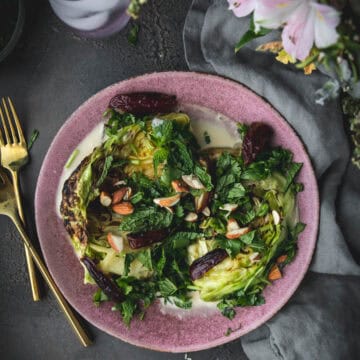 overhead shot of green grilled cabbage on a plate with tahini sauce and charred dates