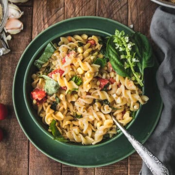 bowl of creamy sweet corn pasta with basil and tomatoes shot from overhead