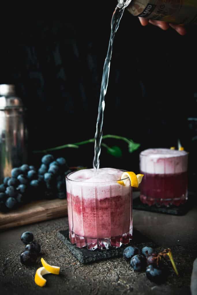 sparkling water pouring into a concord grape gin fizz cocktail