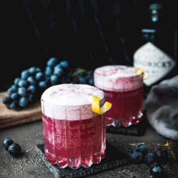 two glasses of concord grape gin fizz cocktails with a lemon twist