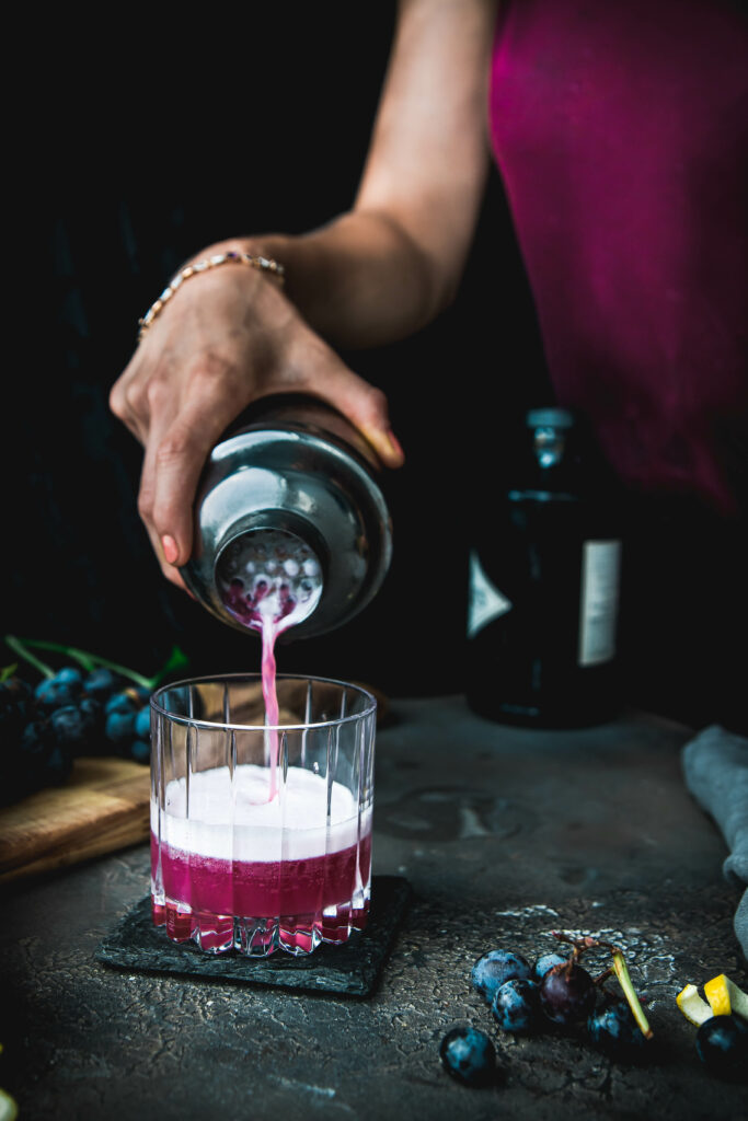 person pouring purple gin fizz into a rocks glass
