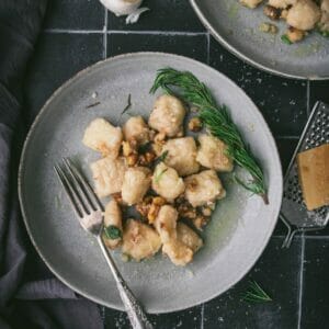 one bowl with a fork of vegan leftover mashed potato gnocchi in an herb butter sauce on a black tile table