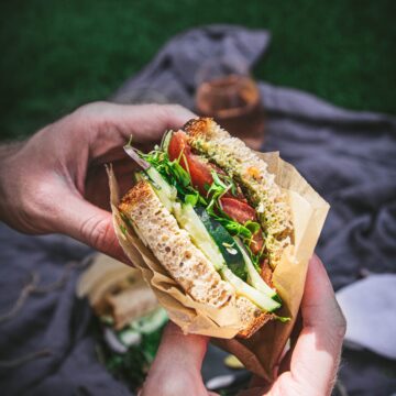 hands holding a vegan california veggie sandwich over a picnic