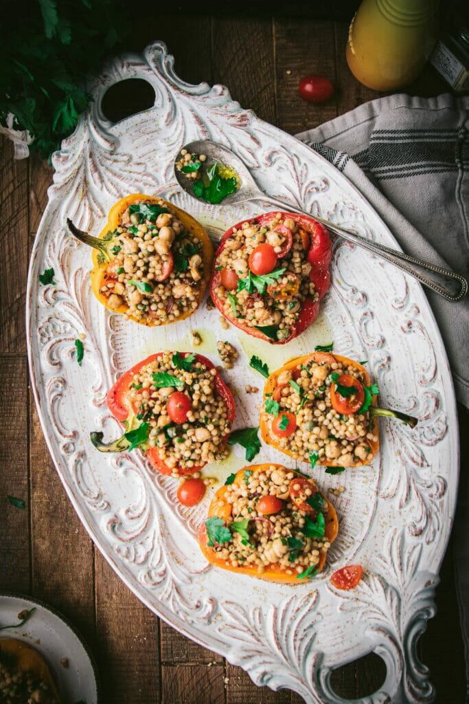 overhead shot of a plate of five greek couscous stuffed peppers on a white platter with a spoon