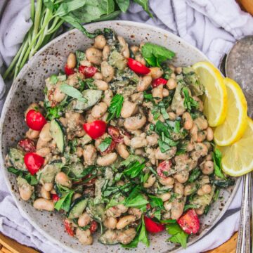 close up shot of pesto white bean salad with cherry tomatoes and cucumbers next to a bouquet of basil