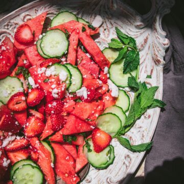 a high angle shot of watermelon, cucumber, and feta salad next to a bottle of water on a white tray