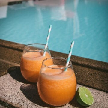 two glasses of melon agua fresca next to a pool