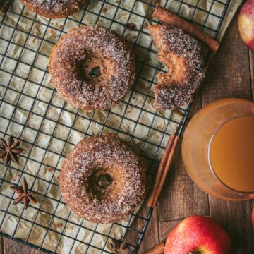 glass of apple cider next to baked apple cider donuts