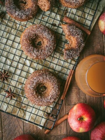 glass of apple cider next to baked apple cider donuts