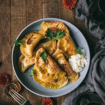 plate of vegan pumpkin pierogi with yogurt on wood table